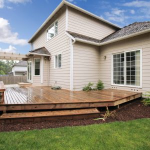 Large beige painted house with porch from the backyard with grass and mulch.