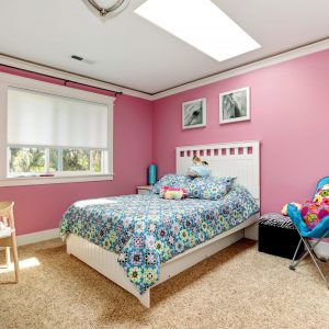 Gentle girls bedroom with white bed and pink colored painted walls. View of bed with blue bedding,blue chair