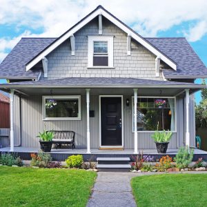Small old house with entrance porch decorated with antique bench. Front yard has lawn and flower beds