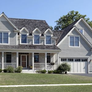 Suburban light grey painted home with porch and cedar roof.